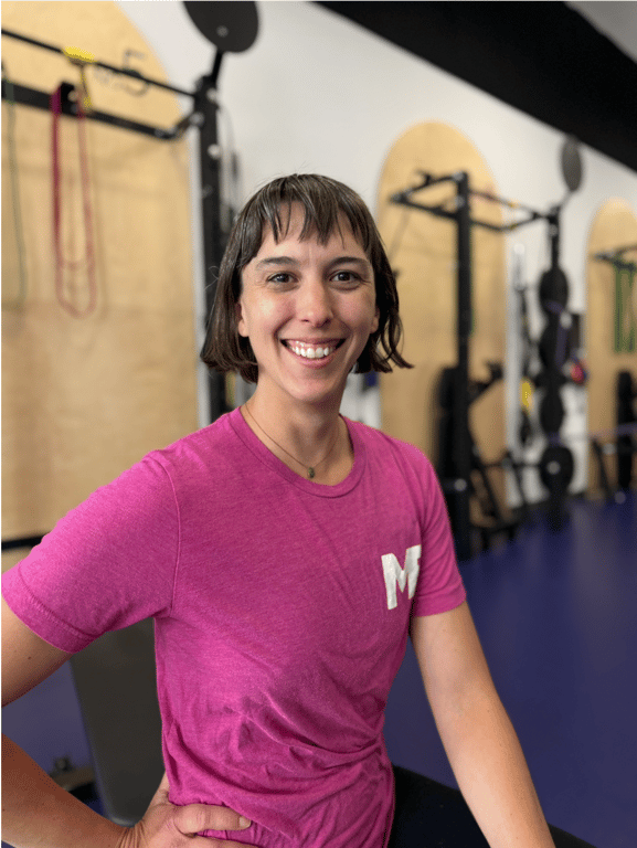 Lindsay, coach at Studio ME Fitness, smiling in a pink Studio ME shirt in the Northeast Minneapolis studio.